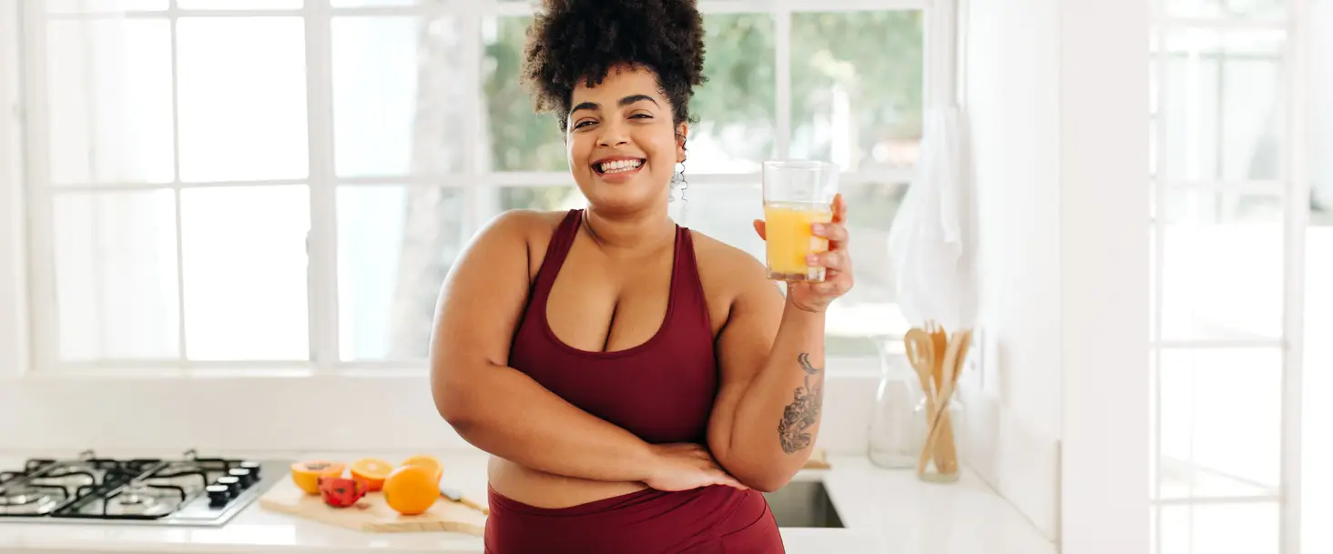 curvy black woman in fitness clothing drinking orange juice for nutrition